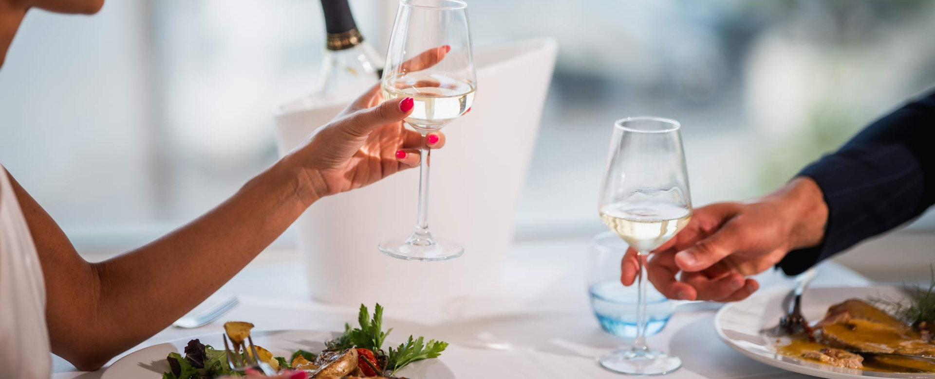 Two people toast with white wine, elegant and intimate atmosphere.