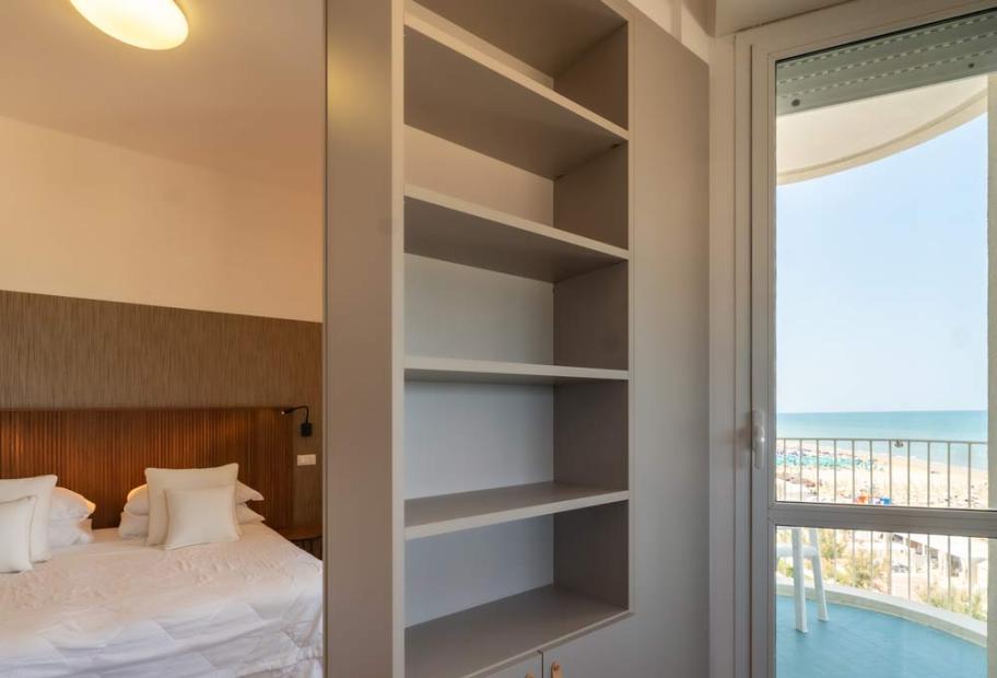 Bright room with sea view, cozy bed, and empty shelf.
