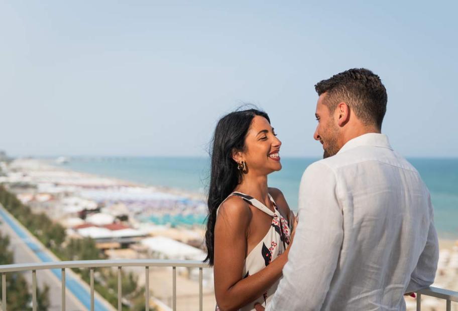 Happy couple embracing on a balcony, ocean view, romantic and serene atmosphere.