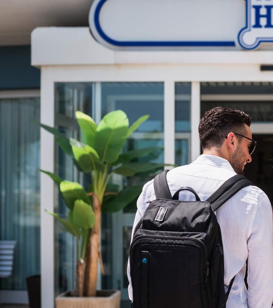 Uomo con zaino, sorridente, entra in hotel, atmosfera estiva e accogliente.
