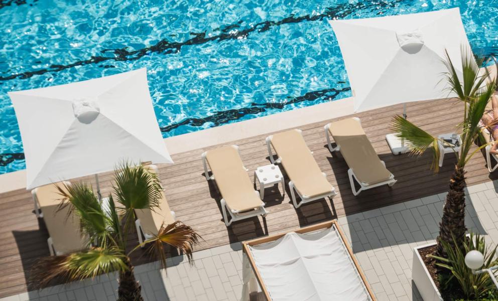 Piscina azzurra, sdraio sotto ombrelloni bianchi, relax estivo e palme.